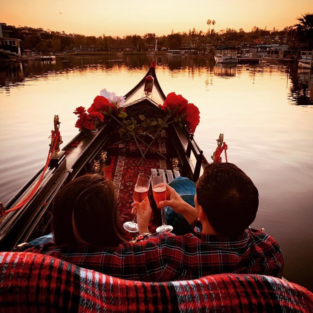 Couple enjoying a romantic gondola ride at sunset, holding champagne glasses, surrounded by roses and a scenic waterfront in San Diego.