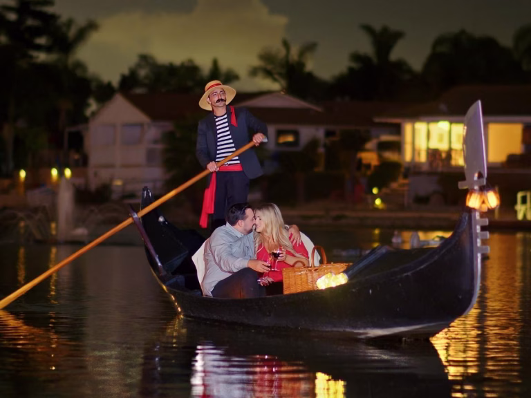 Couple enjoying a romantic gondola ride at night on Lake San Marcos, with a gondolier, picnic basket, and cozy atmosphere, reflecting a perfect anniversary or proposal setting in Carlsbad, CA.
