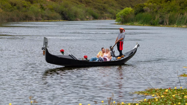 Couple enjoying a romantic gondola ride on a serene lake in Carlsbad, surrounded by lush greenery and calm waters, ideal for marriage proposals.