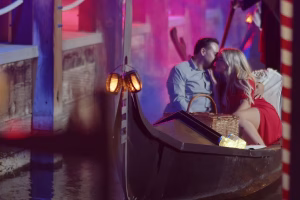 Couple sharing a romantic kiss on a gondola, surrounded by colorful lights, representing a dreamy dining experience on a San Diego dinner cruise.