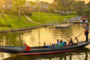 Gondola cruising on a serene lake during sunset, showcasing a couple enjoying a romantic experience, surrounded by lush greenery and calm waters, reflecting the ambiance of Black Swan Gondola's dinner cruise offerings.